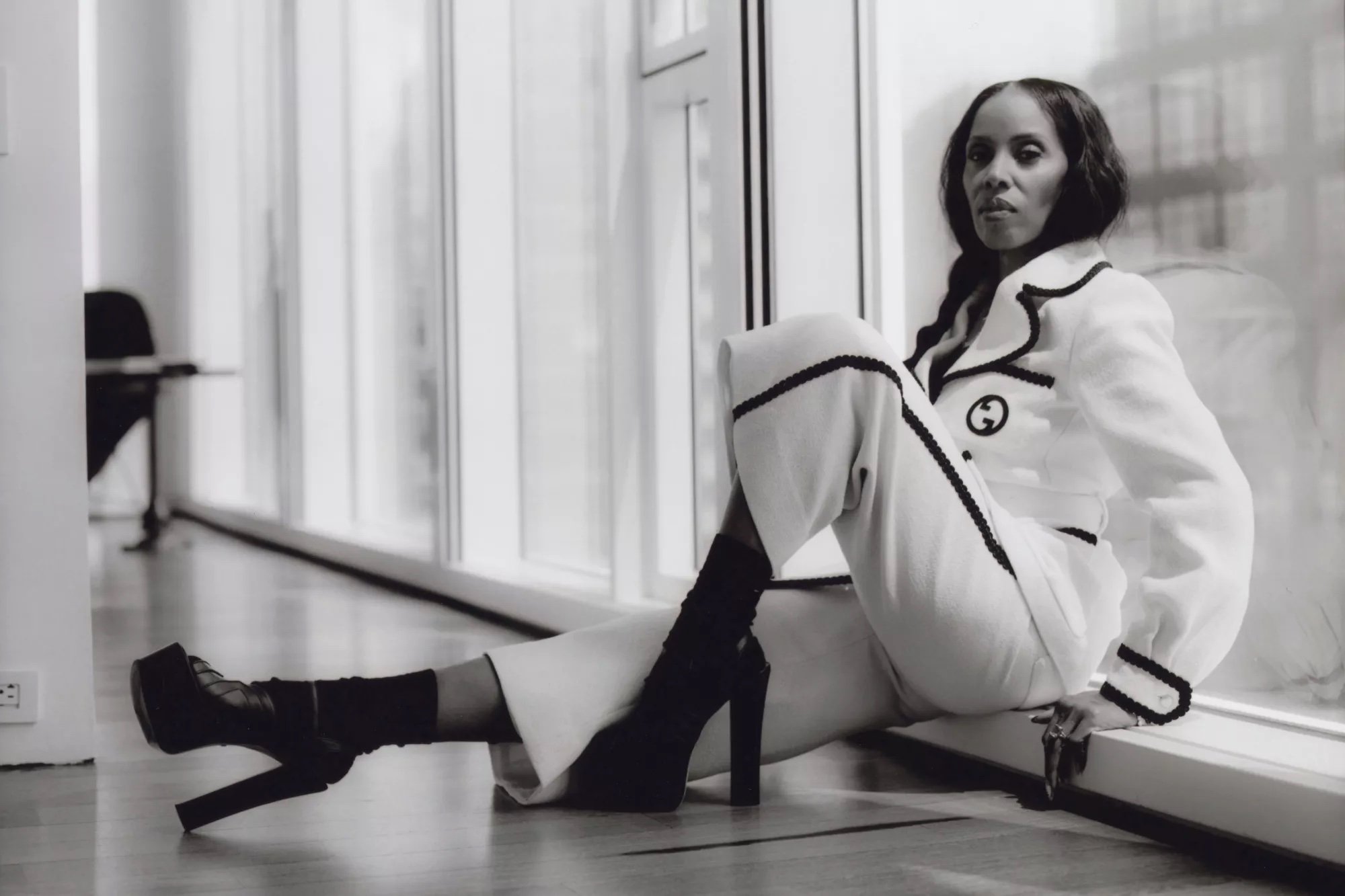Black woman seated near bright windows wearing a white suit with dark trim and platform heels in New York by Renee Sanganoo