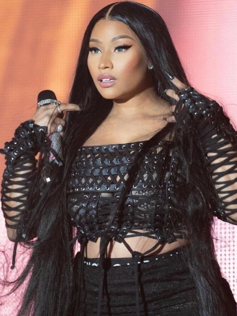 Singer Nicki Minaj performs onstage, wearing a black, lace-up outfit and long black hair, holding a microphone. Entertainment, celebrity portrait.