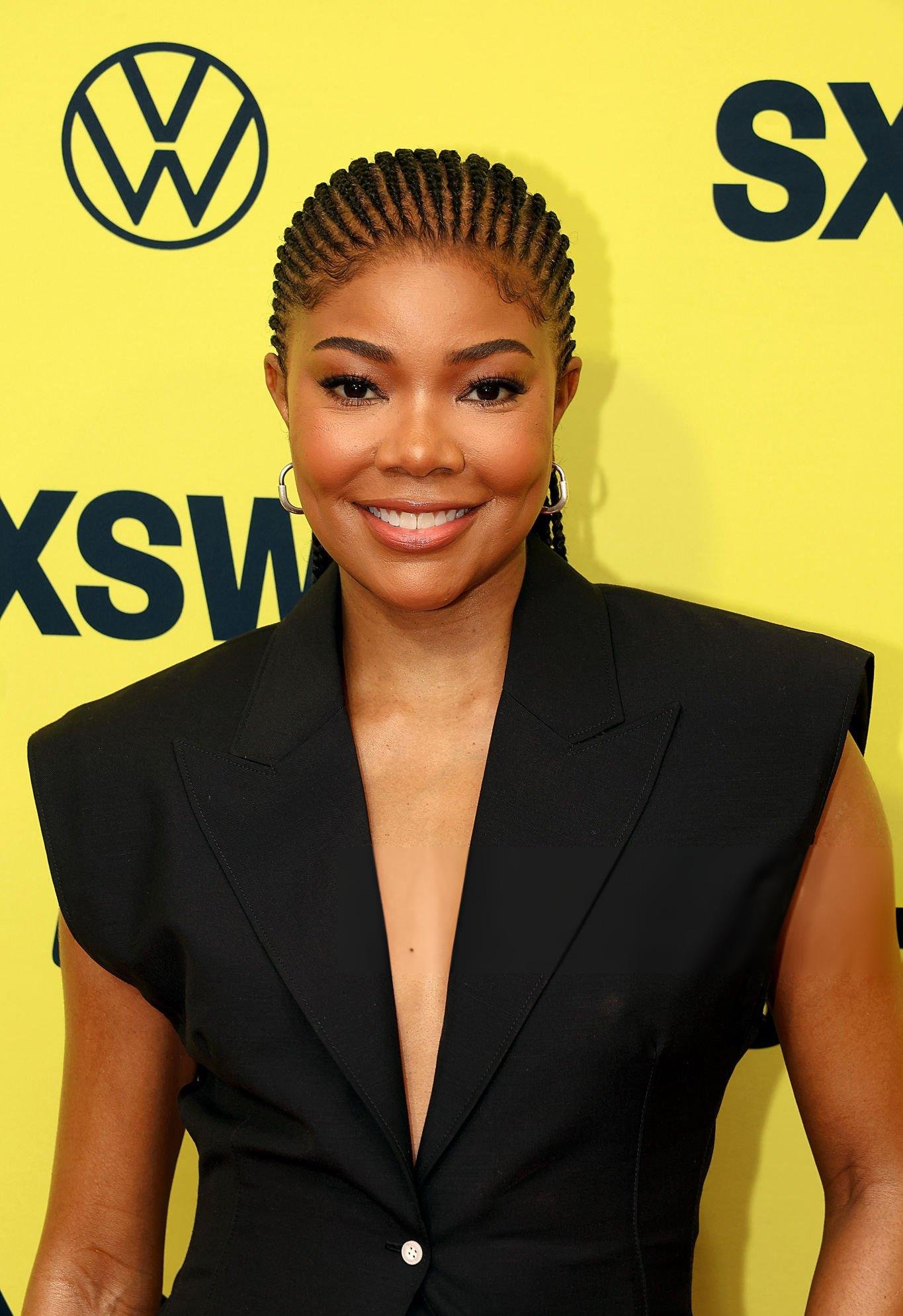 Portrait of a smiling woman with braided hair, wearing a black sleeveless blazer against a bright yellow SXSW branded backdrop.