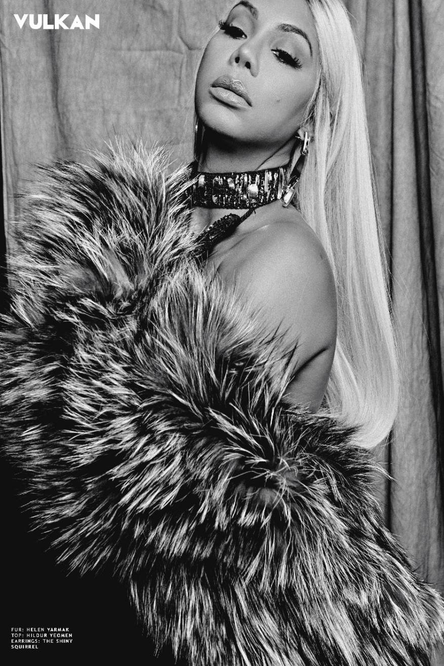 Black and white editorial portrait of a woman wearing a fluffy faux fur coat and a chunky studded choker necklace.