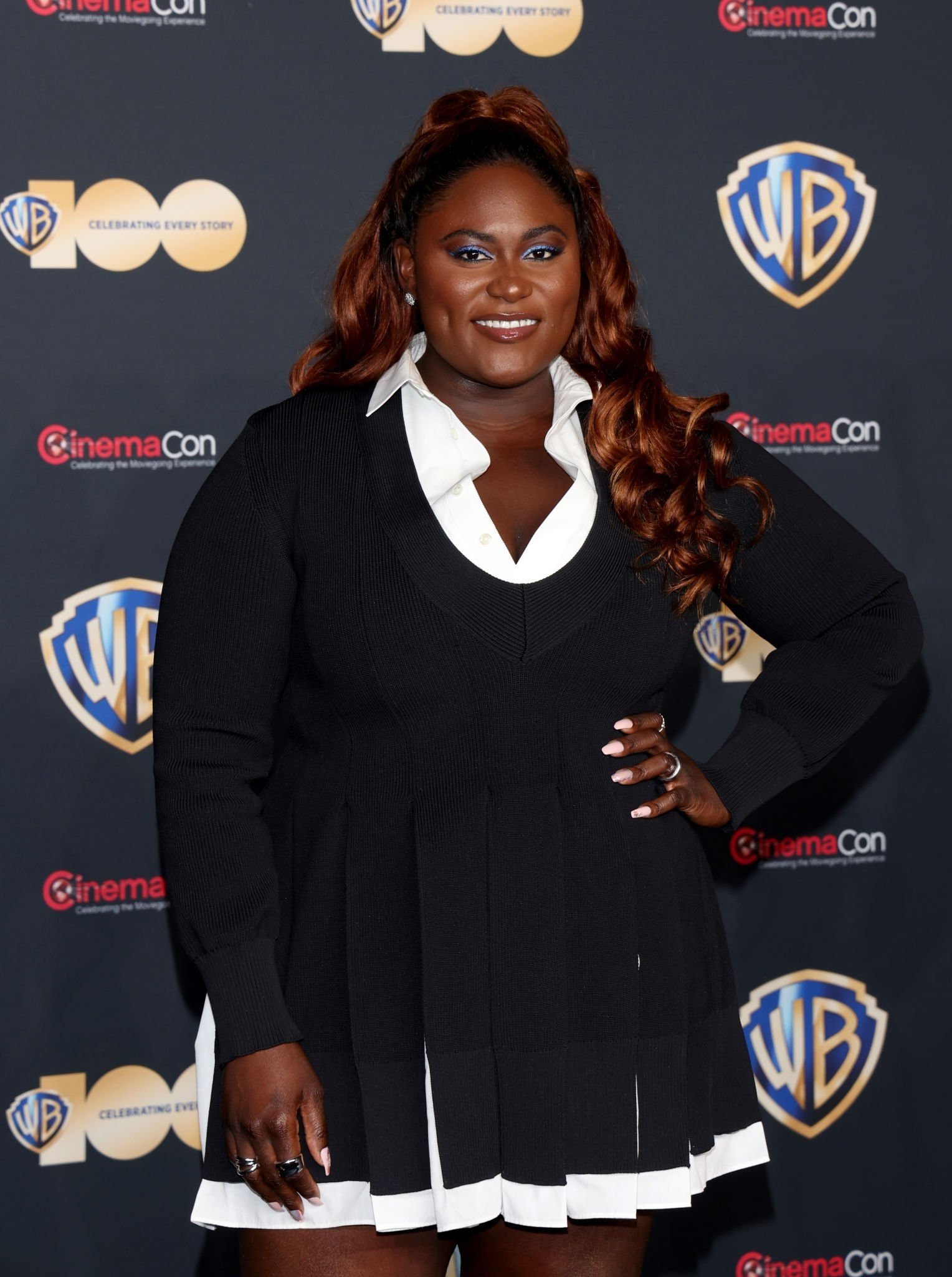 Headshot of a smiling woman with auburn hair wearing a black and white dress, posing in front of a branded CinemaCon backdrop.