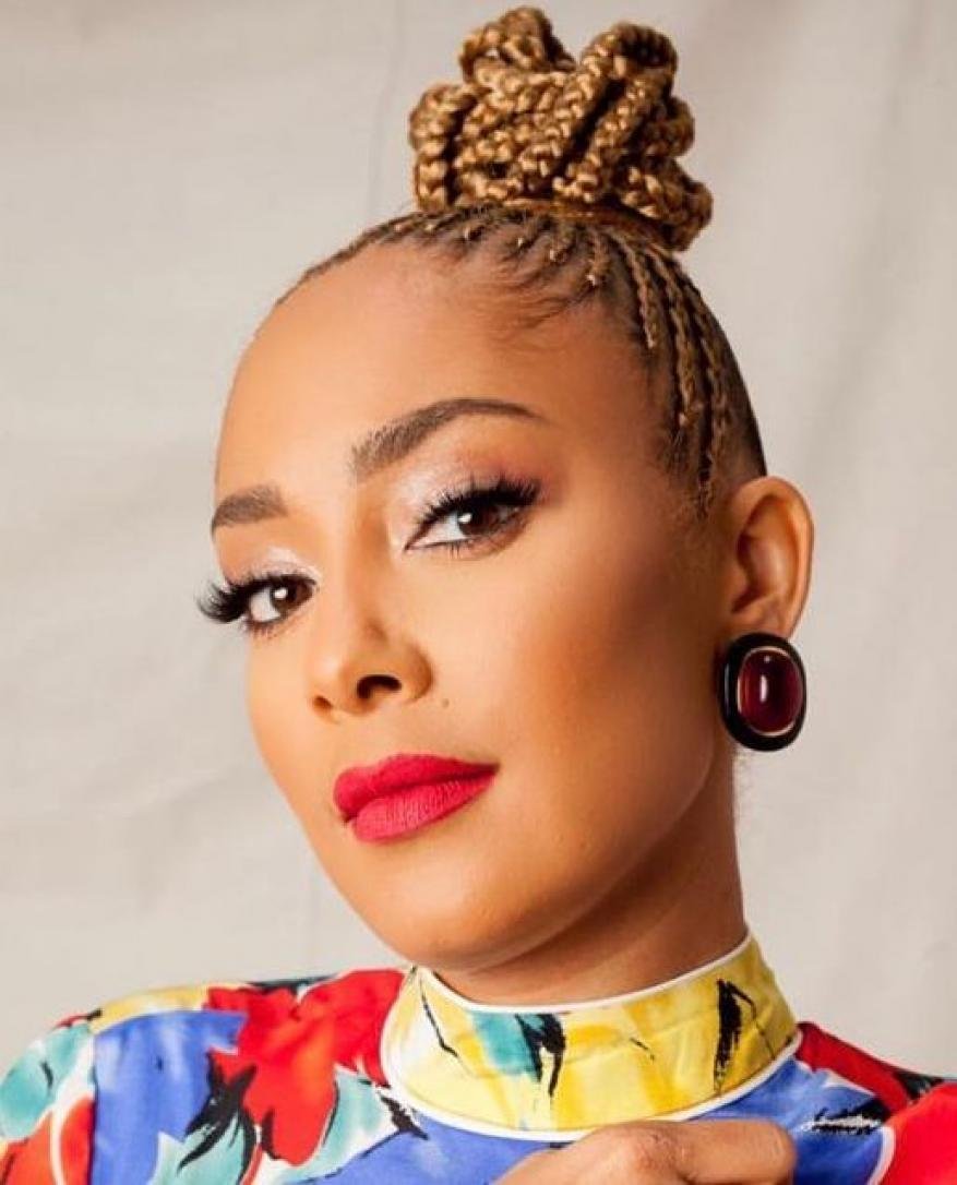 Close-up studio portrait of a smiling adult woman with braided hair in a top-knot, wearing a colorful shirt and red lipstick.