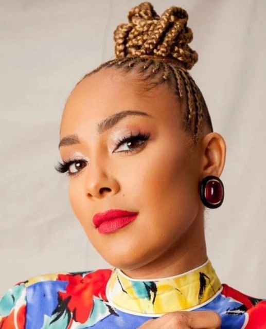 Close-up studio portrait of a smiling adult woman with braided hair in a top-knot, wearing a colorful shirt and red lipstick.