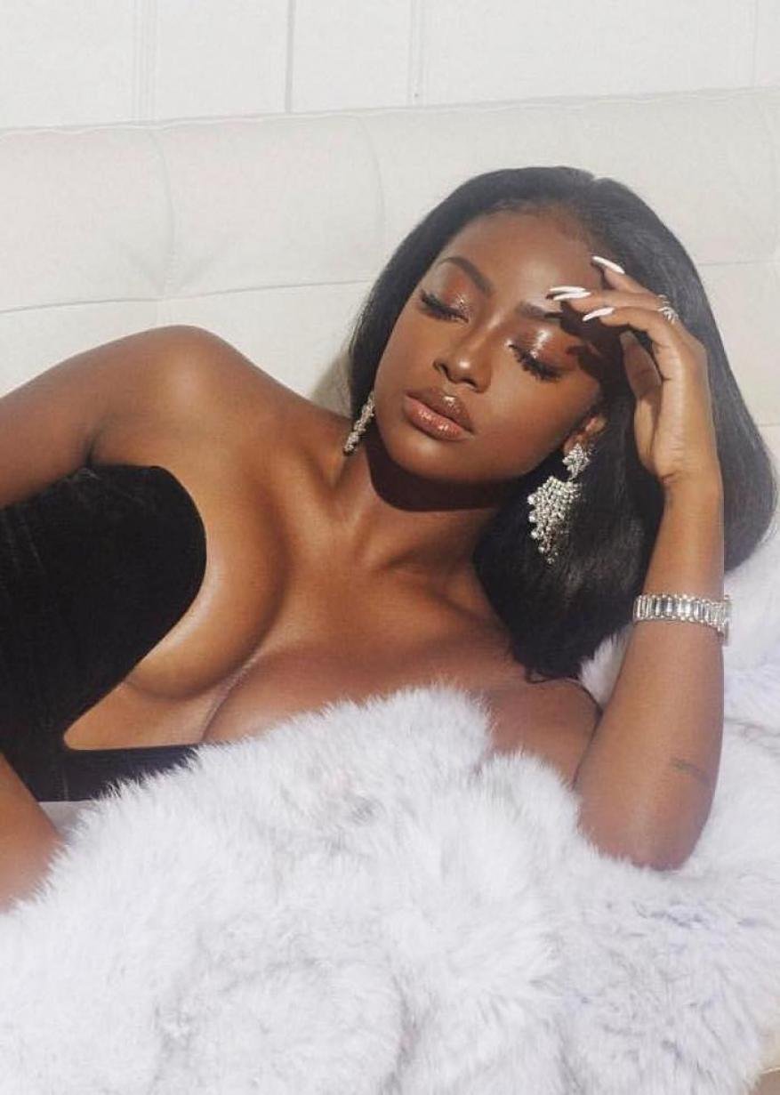 Glamorous woman with dark hair poses while lying on white fur. She wears dangling earrings and a crystal bracelet, illuminated by soft lighting.