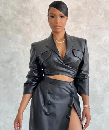 Portrait of an adult woman with dark hair in a sleeked style, wearing a black faux leather jacket and skirt against a neutral background.