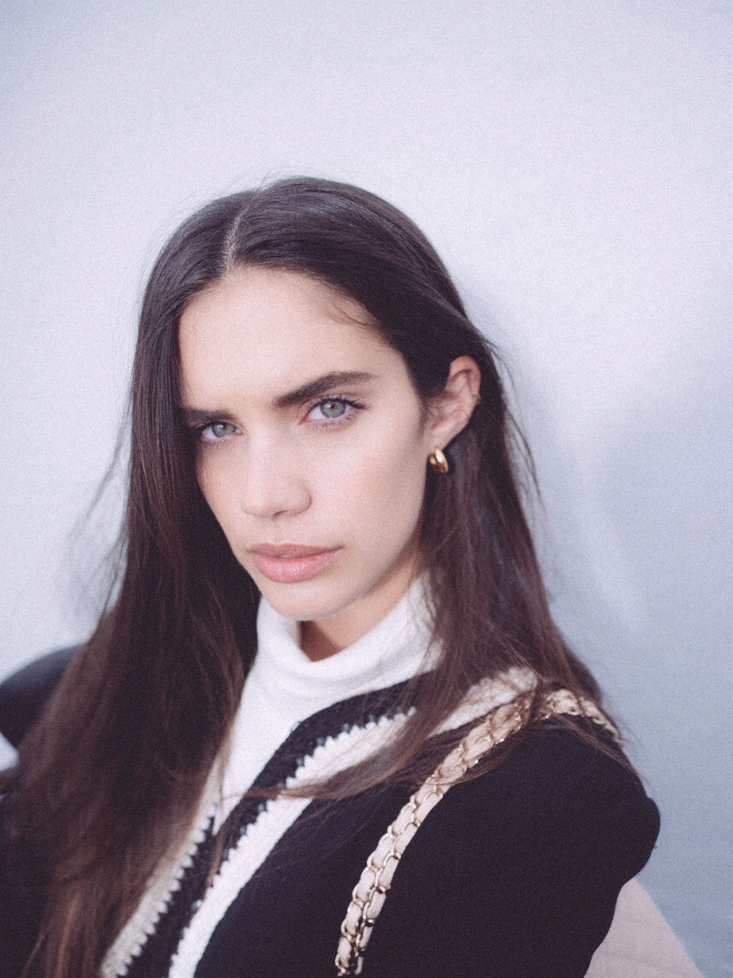 Portrait of an attractive brunette adult female with fair skin and grey eyes, wearing a knit top, posing indoors against a light background.