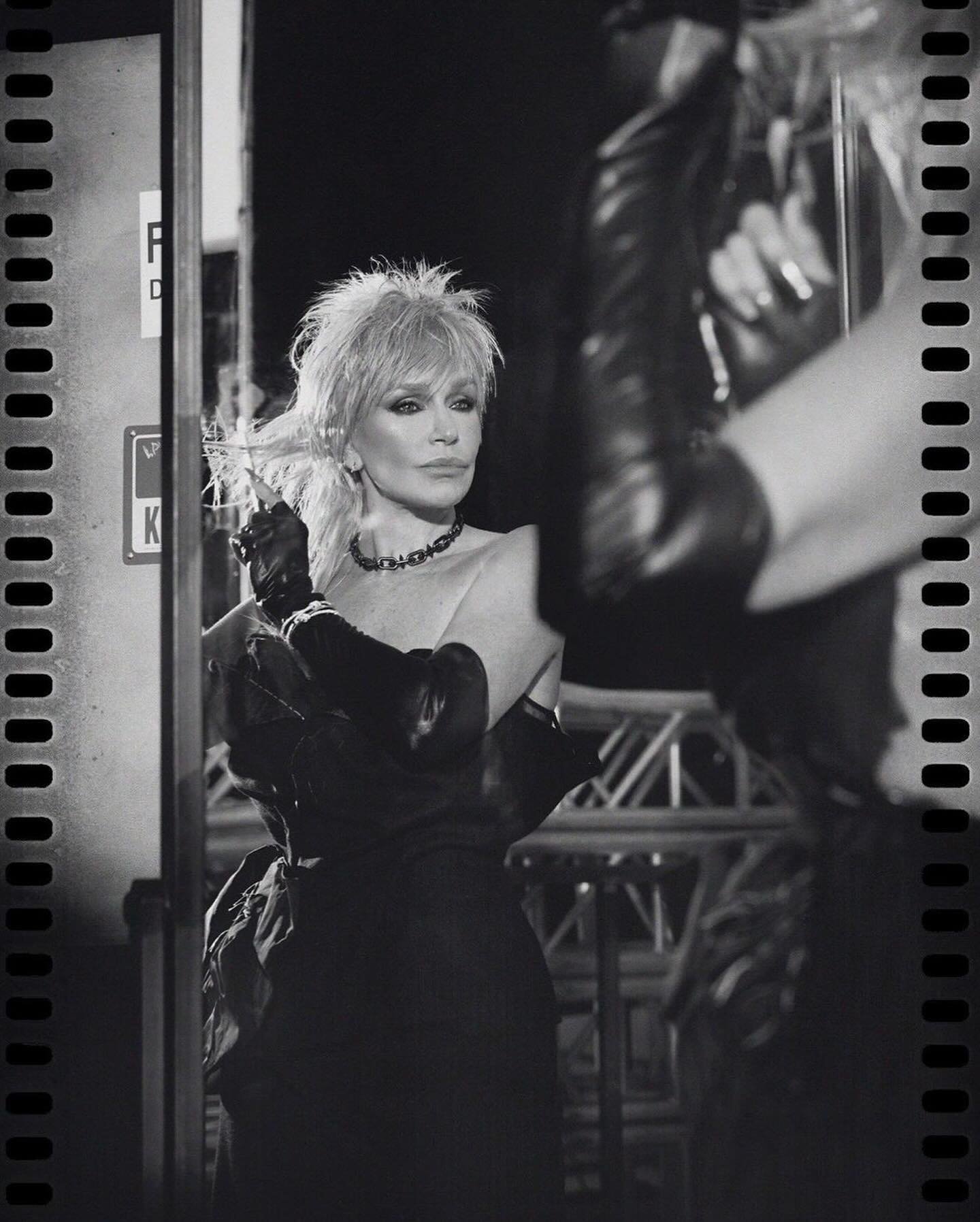 Elegant, mature woman with blonde hair and black dress smoking with someone taking her picture in black and white with film border.