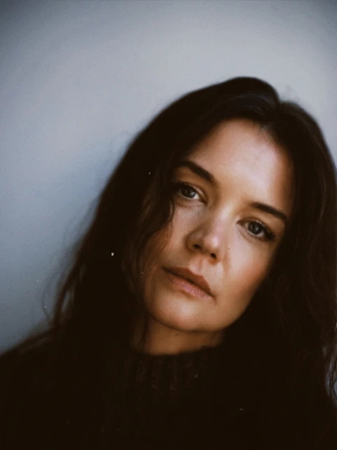 Portrait of an adult female with long brown hair and neutral facial expression, wearing a dark sweater in a neutral setting.