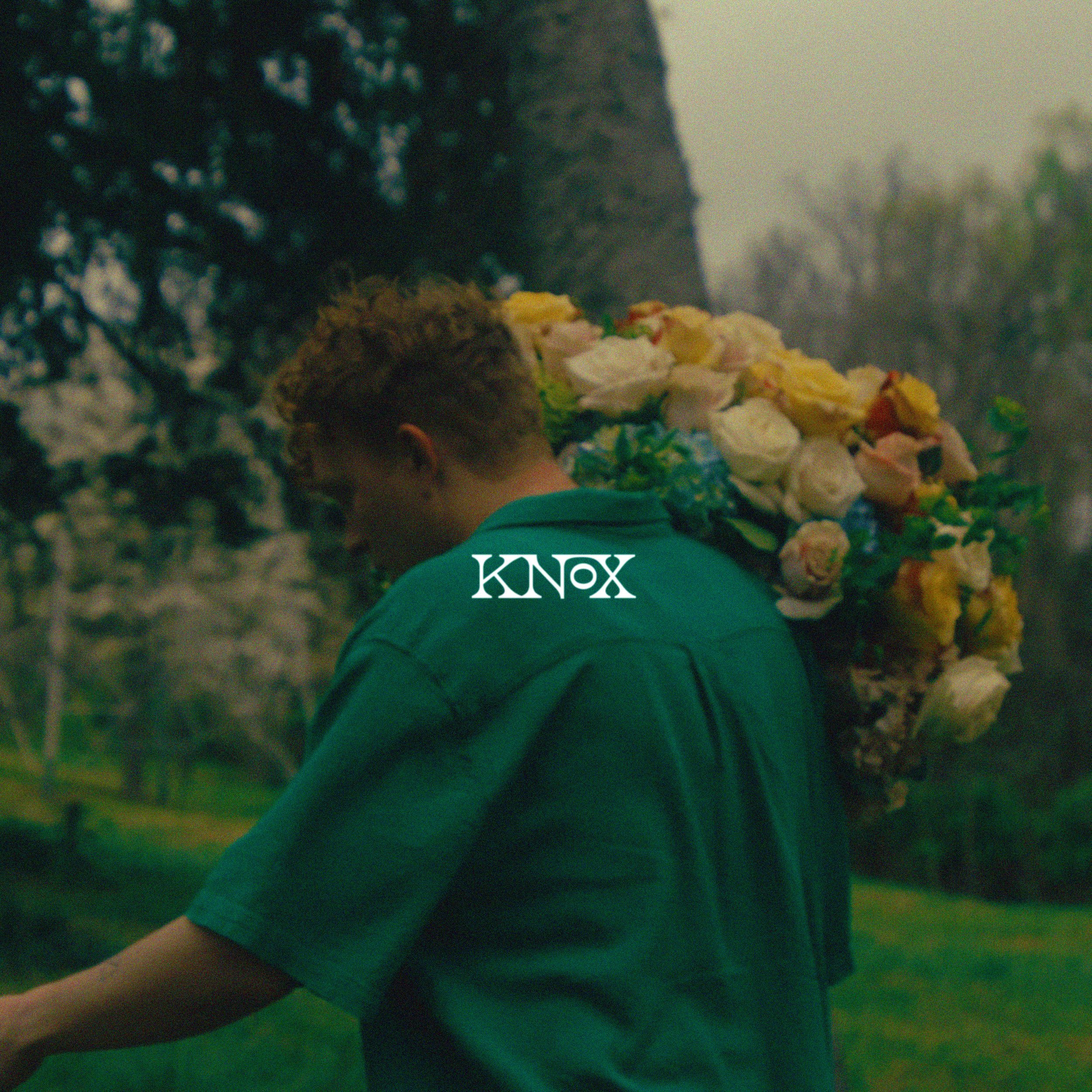 Man carries bouquet of flowers on shoulder outdoors in green shirt. The scene is slightly blurred, giving an impressionistic feel.