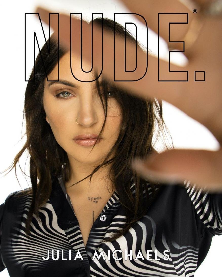 Close-up portrait of Julia Michaels looking at the camera with a hand held up and a zebra patterned shirt against a white background.