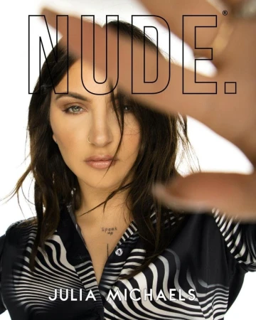 Close-up portrait of Julia Michaels looking at the camera with a hand held up and a zebra patterned shirt against a white background.