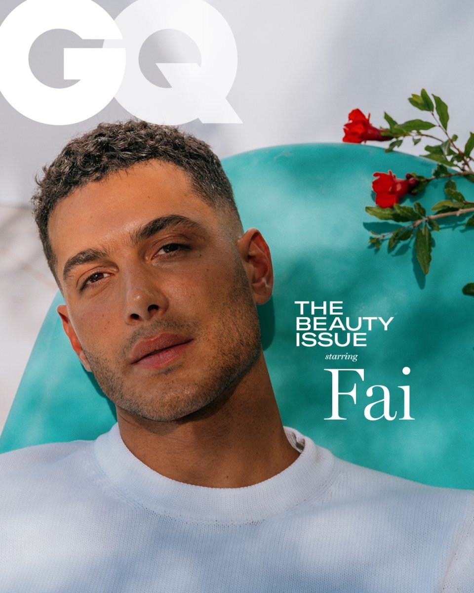 Close-up of a handsome man with short curly hair in a white shirt, part of a GQ Beauty Issue cover against an aqua background.