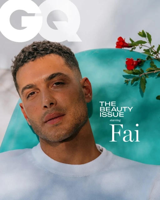 Close-up of a handsome man with short curly hair in a white shirt, part of a GQ Beauty Issue cover against an aqua background.