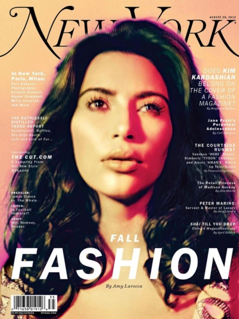 Close-up magazine cover of Kim Kardashian with dark wavy hair, wearing jewelry and makeup, against a blurred editorial background.