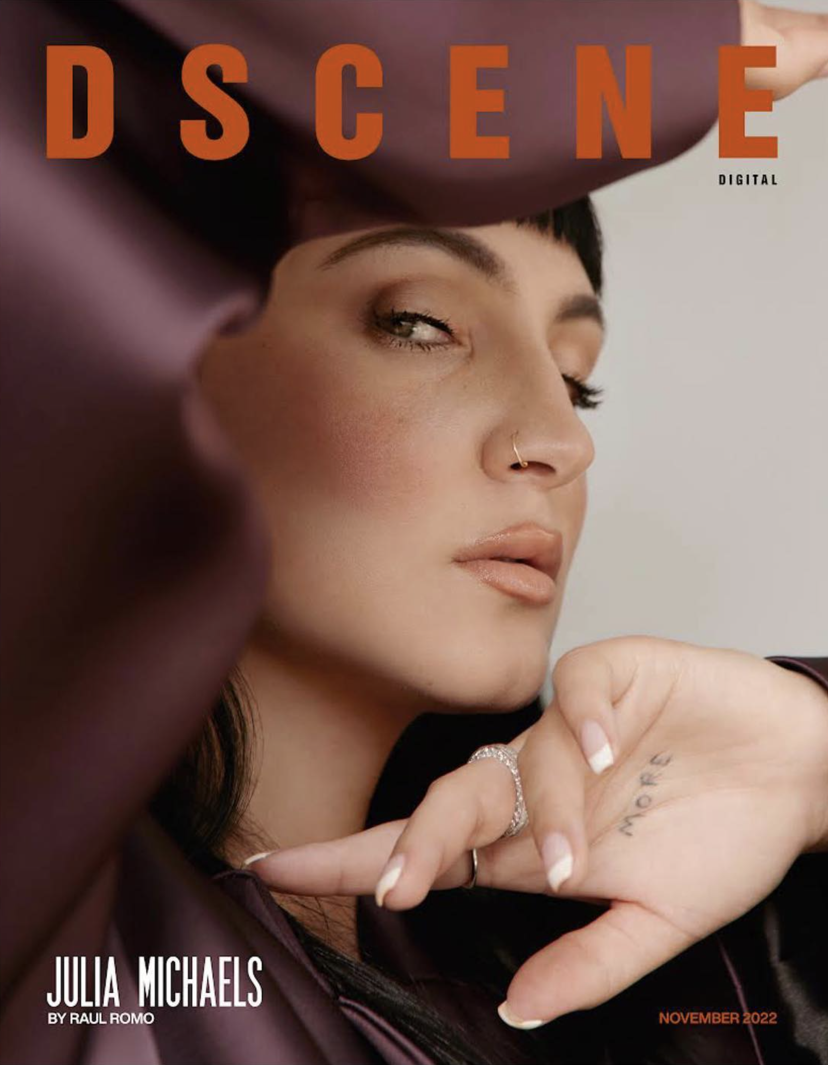 Julia Michaels poses on the cover of DSCENE magazine, showcasing a plum satin outfit, a ring, natural makeup, and a distinctive hand tattoo.