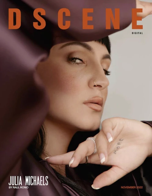 Julia Michaels poses on the cover of DSCENE magazine, showcasing a plum satin outfit, a ring, natural makeup, and a distinctive hand tattoo.