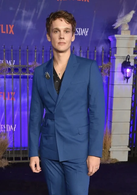 Portrait of a man in a blue suit at a premiere event with a backdrop featuring event signage and lighting, creating a formal atmosphere.