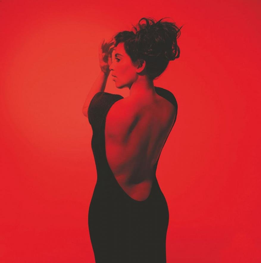 Elegant woman in a black dress against a red backdrop, showcasing her bare back and an updo hairstyle in a studio setting.