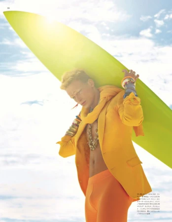 Man in a bright yellow blazer holding a chartreuse surfboard against a bright sky, styled by Rob Scheppy.