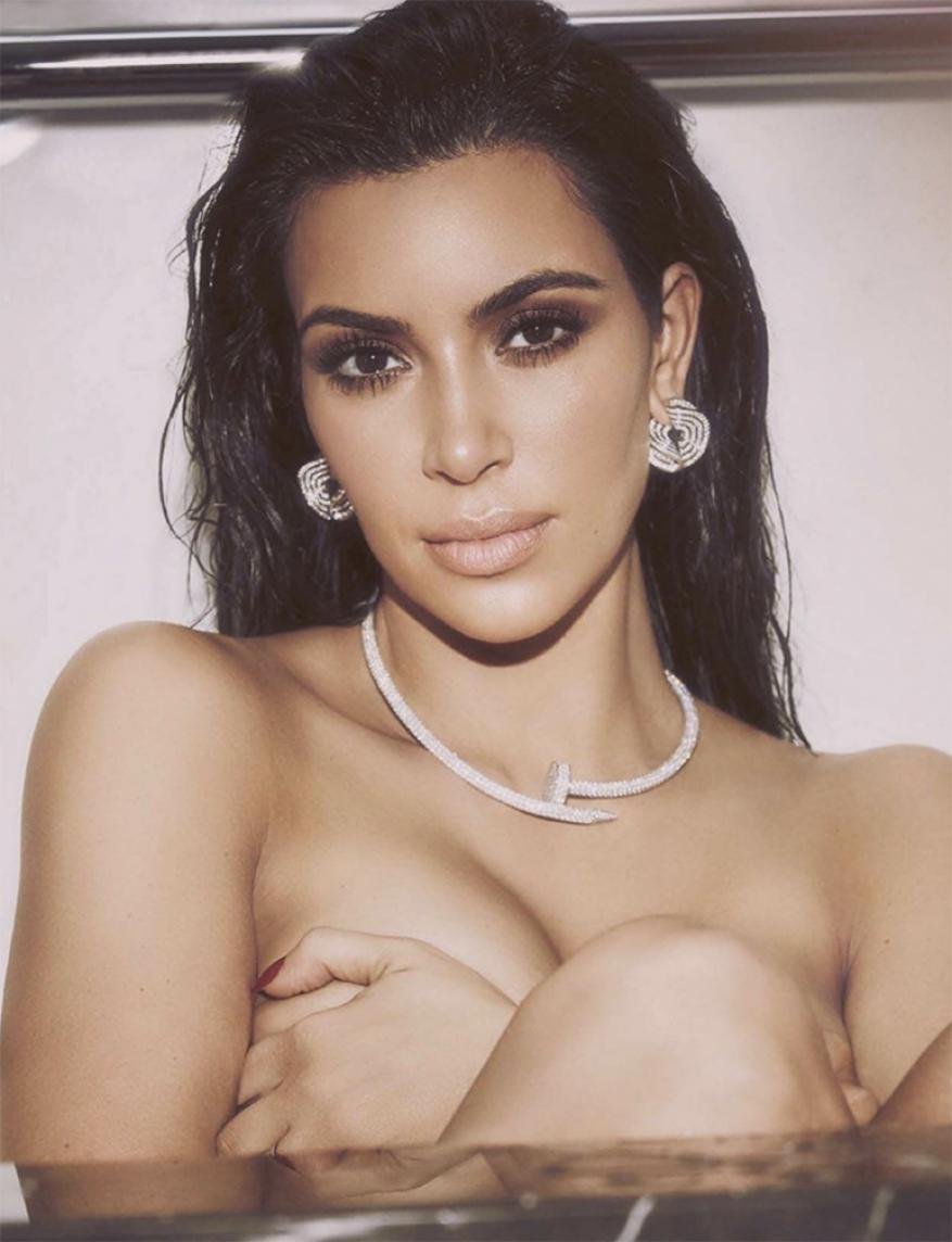 Close-up portrait of Kim Kardashian wearing diamond jewelry and dark smokey eye makeup with wet dark hair.