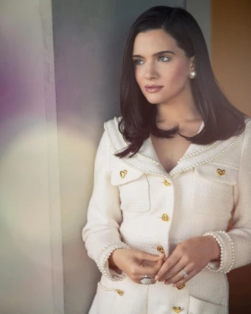 Portrait of an adult female with dark hair wearing a white jacket with gold buttons and pearl trim, looking away from the camera.