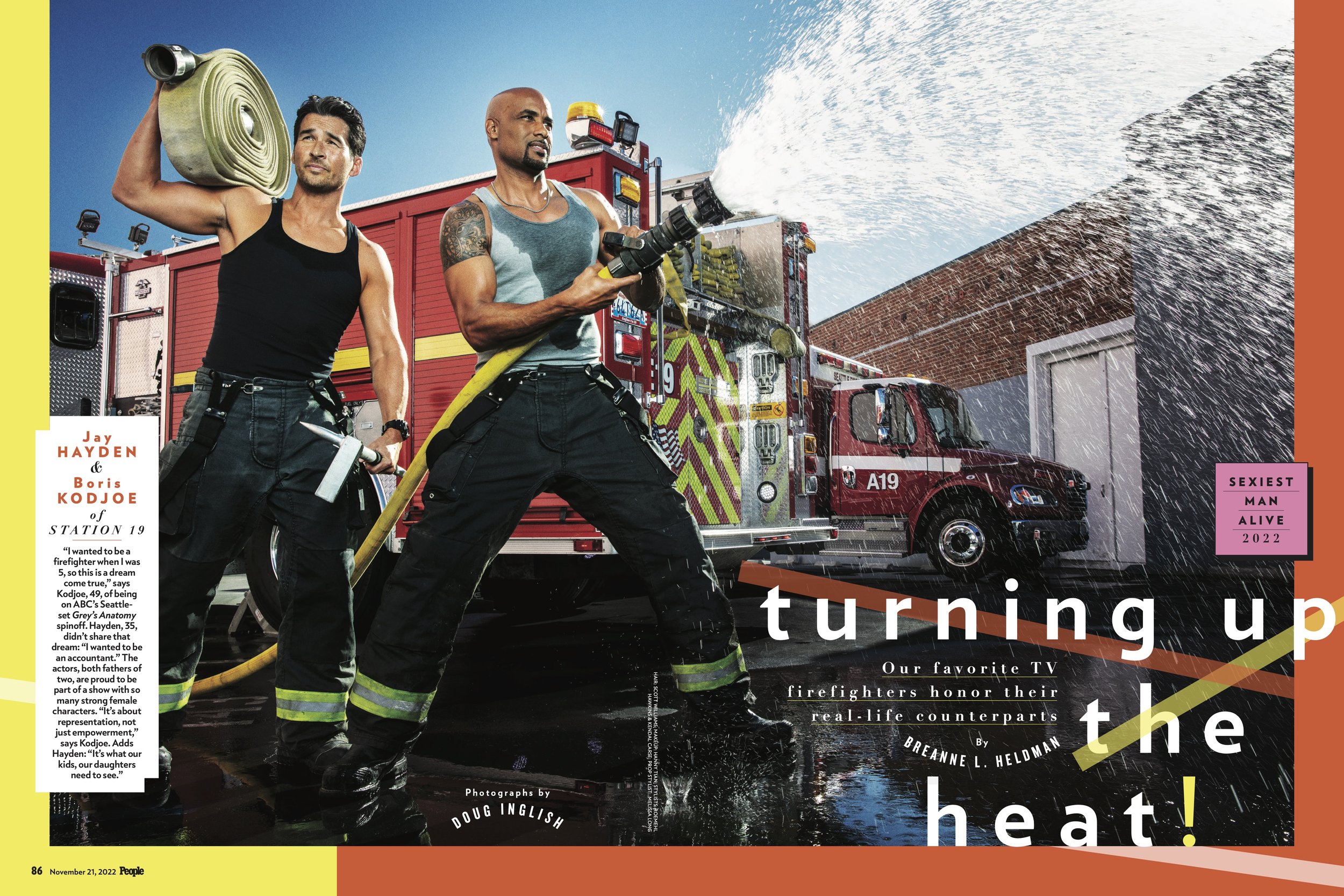 Two firefighters, Jay Hayden and Boris Kodjoe of Station 19, pose in front of a fire truck while one uses a hose to spray water.