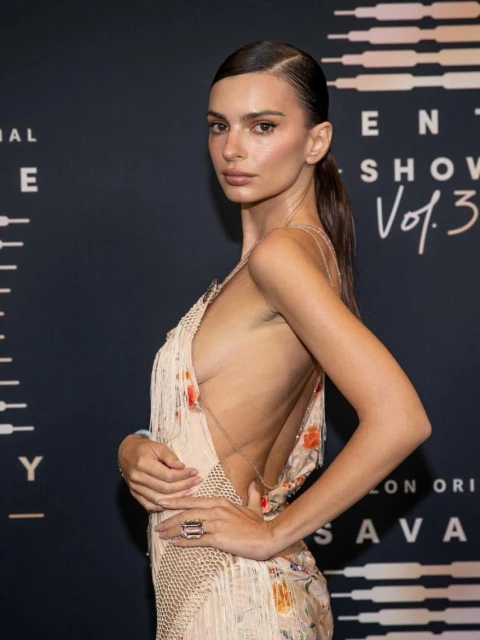 Model Emily Ratajkowski poses in open-backed dress, in a medium studio shot with dramatic lighting at an event for Savage X Fenty.