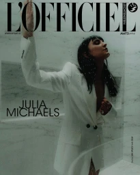 Julia Michaels in a white blazer posing against a marble wall with water droplets for a magazine cover