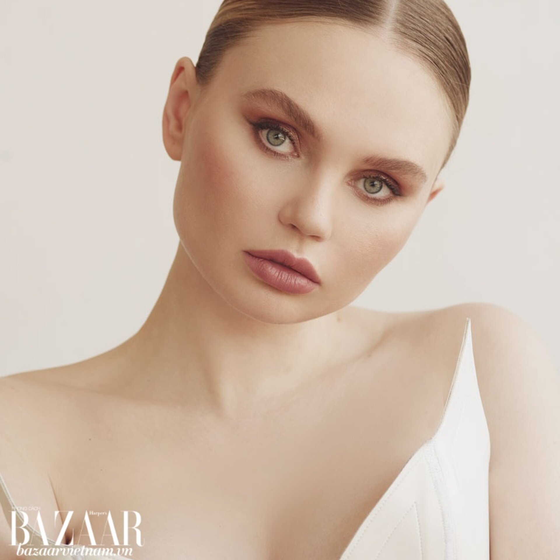 Close-up fashion portrait of a fair-skinned adult female model with clean beauty makeup and hair, posing against a neutral background.