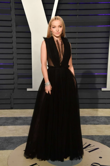 Woman in elegant black dress poses on red carpet at event with light neutral background and modern architectural accents.