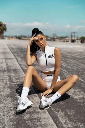 Woman in white crop top and shorts sitting on a rooftop with clear sky