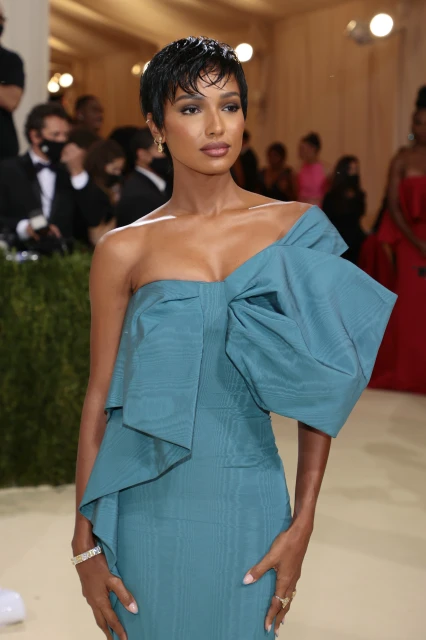 Jasmine Tookes poses in a blue one-shoulder gown with a large bow accent on a red carpet at a celebrity event indoors.