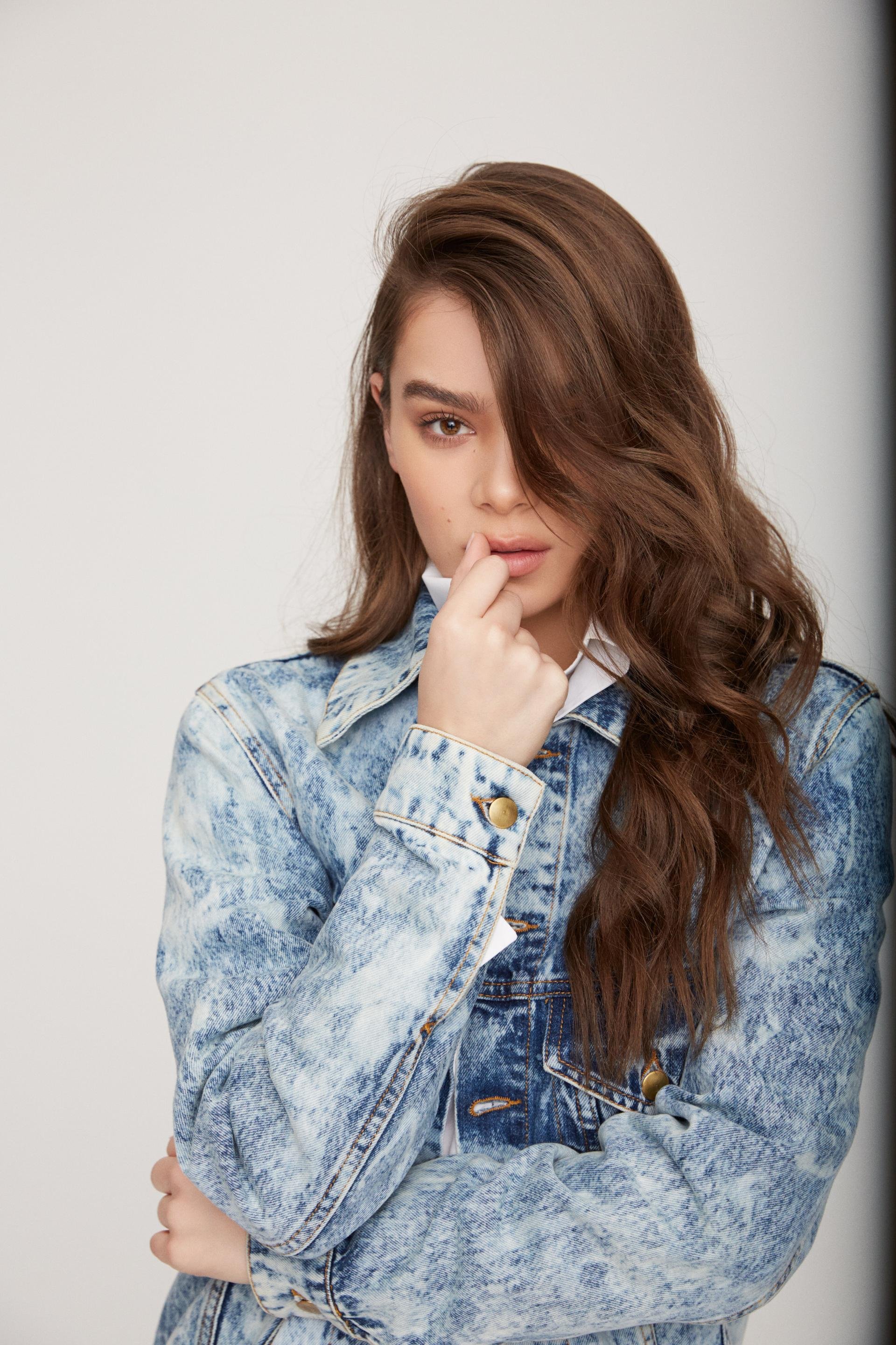 Close-up portrait of a woman with long brown hair wearing an acid-wash denim jacket against a plain background.