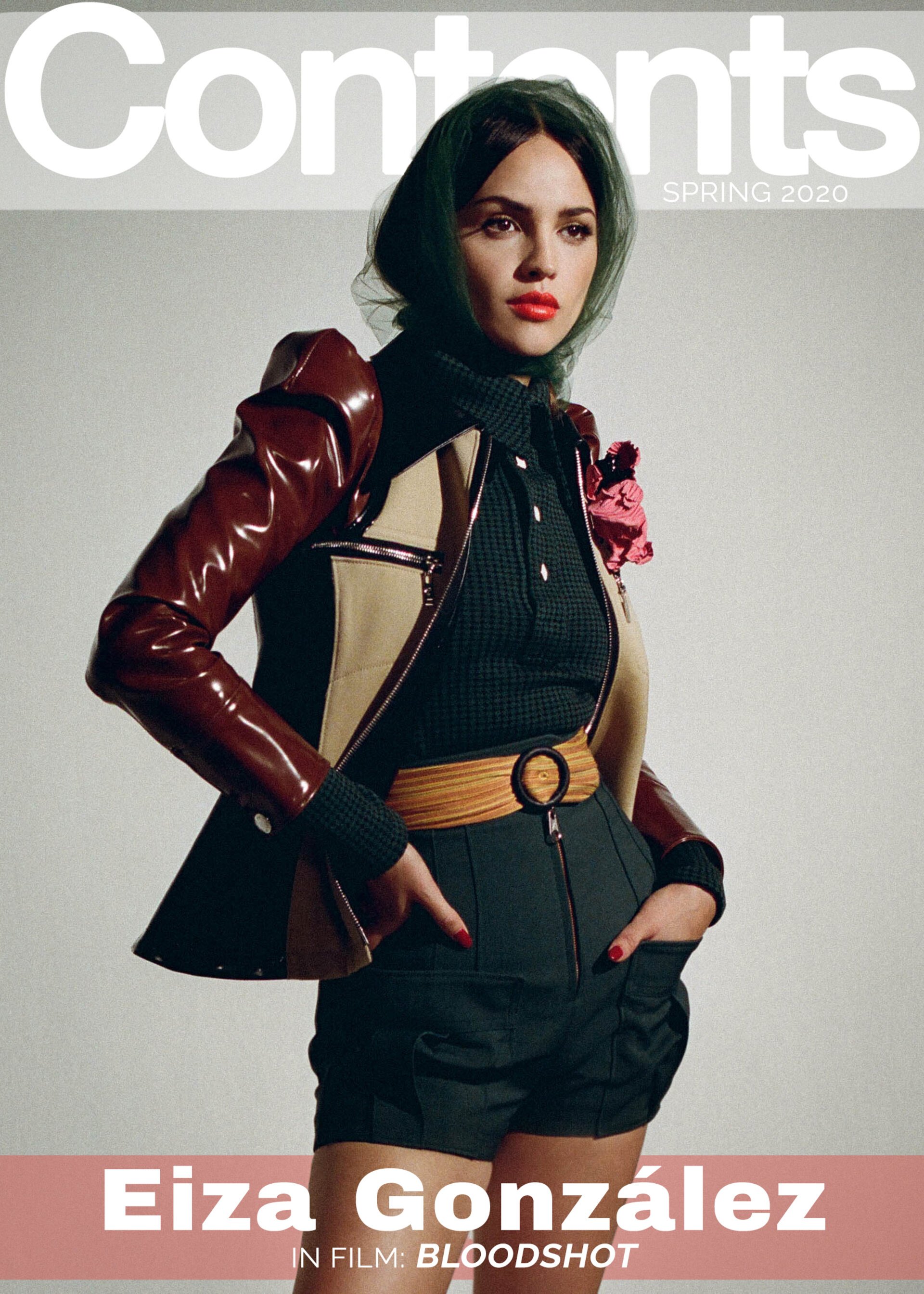 Eiza González on a magazine cover wearing a brown and beige jacket with a black shirt and green headscarf against a gray background.