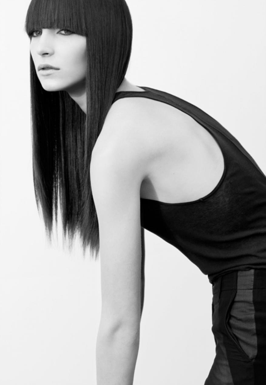 Monochrome studio shot of a model with long, straight black hair, wearing a black tank top and shorts, bending forward slightly.