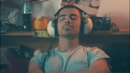 Man wearing headphones and a light t-shirt with eyes closed in an indoor setting by Ryan Randall