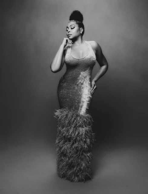 Elegant woman in a silver gown with feathers posing in a studio, showing her stylish updo hair. Monochrome fashion portrait.