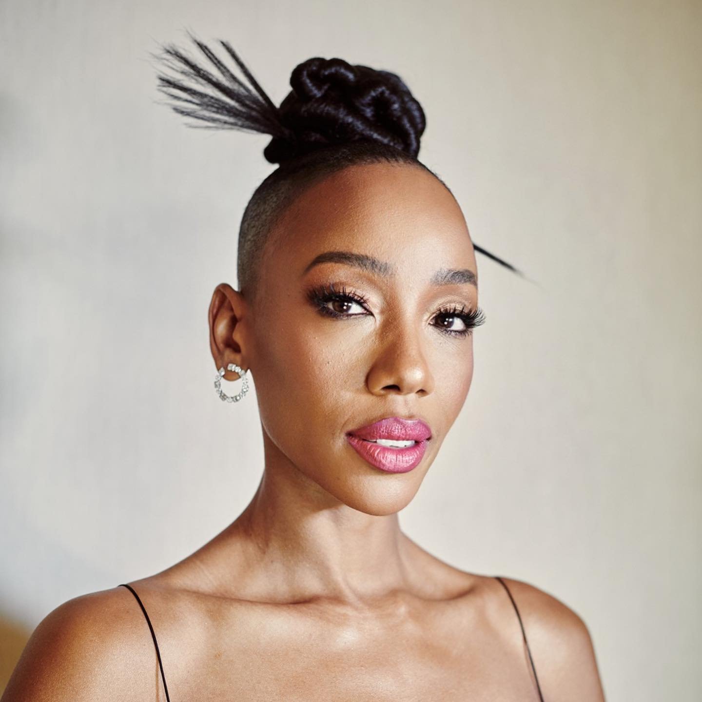 Close-up portrait of a Black woman with an updo hairstyle and neutral makeup. She wears a sleeveless top and hoop earrings.