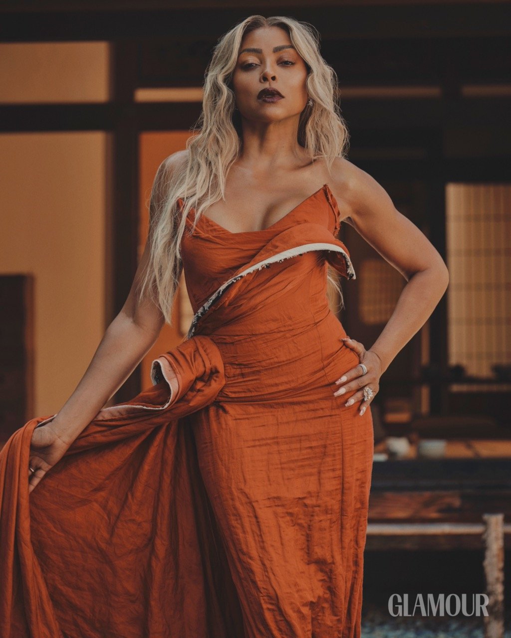 Glamour magazine cover featuring a woman with blonde hair wearing an orange dress posing in front of a brown wooden background.