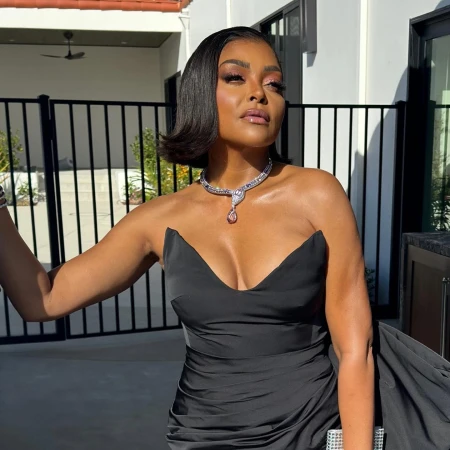 Elegant woman with short black hair wearing a strapless black gown and diamond necklace poses outdoors in front of a building.