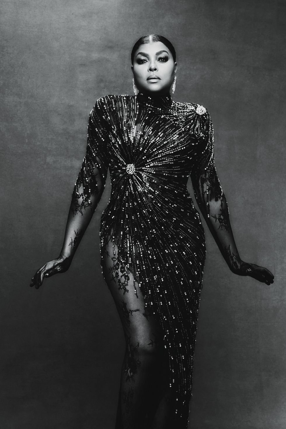 Monochromatic portrait of a woman in a beaded and lace gown, posing against a textured background in a studio setting.