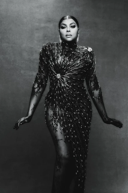 Monochromatic portrait of a woman in a beaded and lace gown, posing against a textured background in a studio setting.