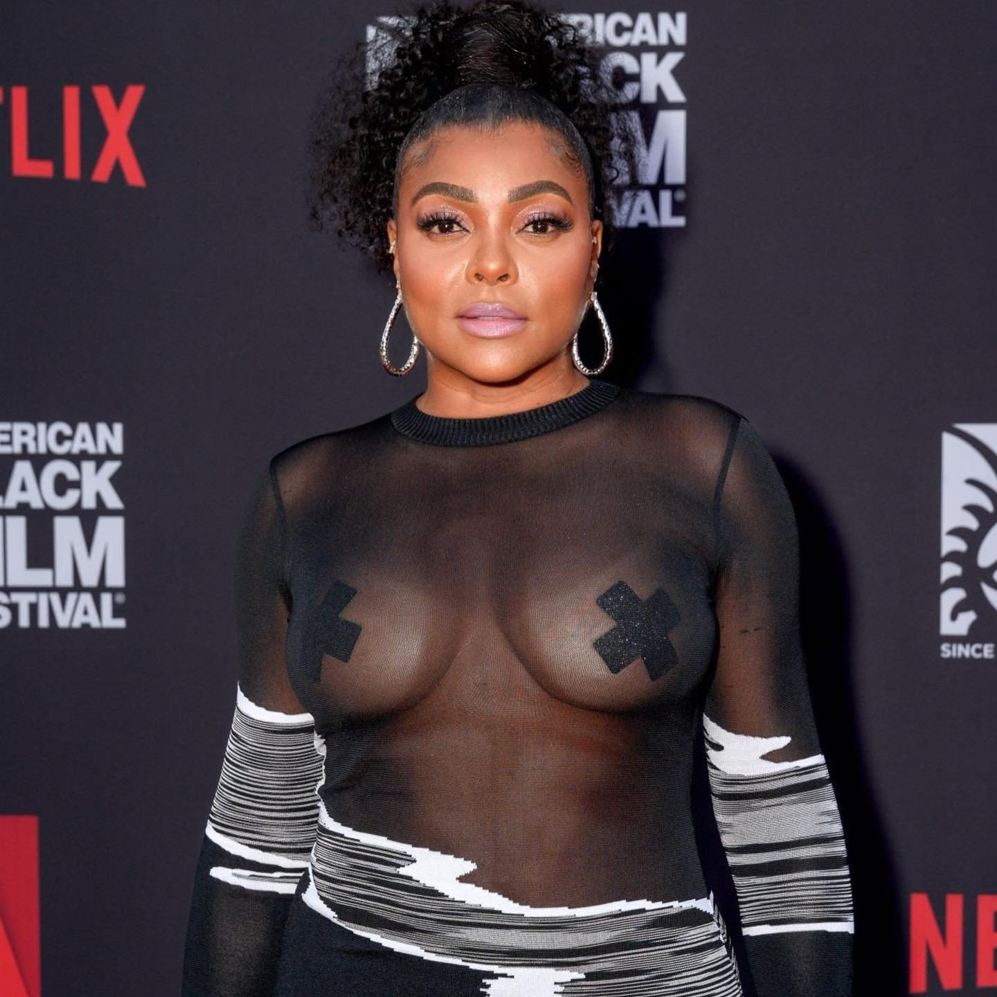 Close-up of Taraji P. Henson at American Black Film Festival, wearing a sheer top, statement earrings, and a curly updo hairstyle.