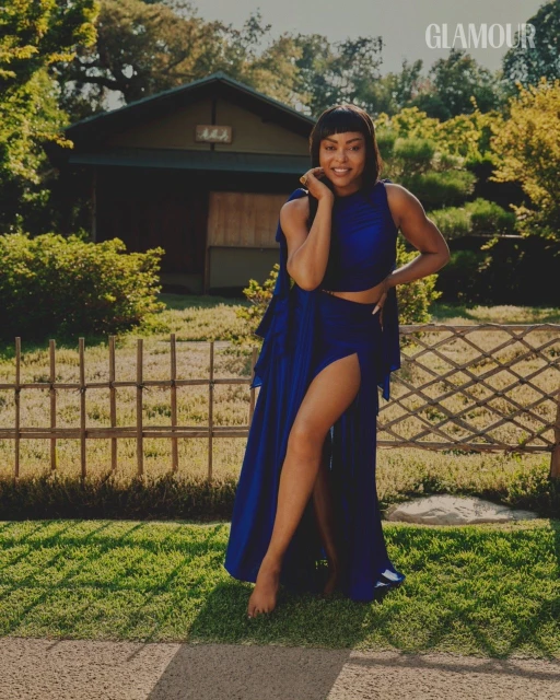 Glamorous woman in a blue high-slit dress poses barefoot in a lush garden setting with a traditional Japanese-style house.