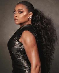 Portrait of a Black woman with long curly hair in a high ponytail wearing a black metallic dress and earrings.