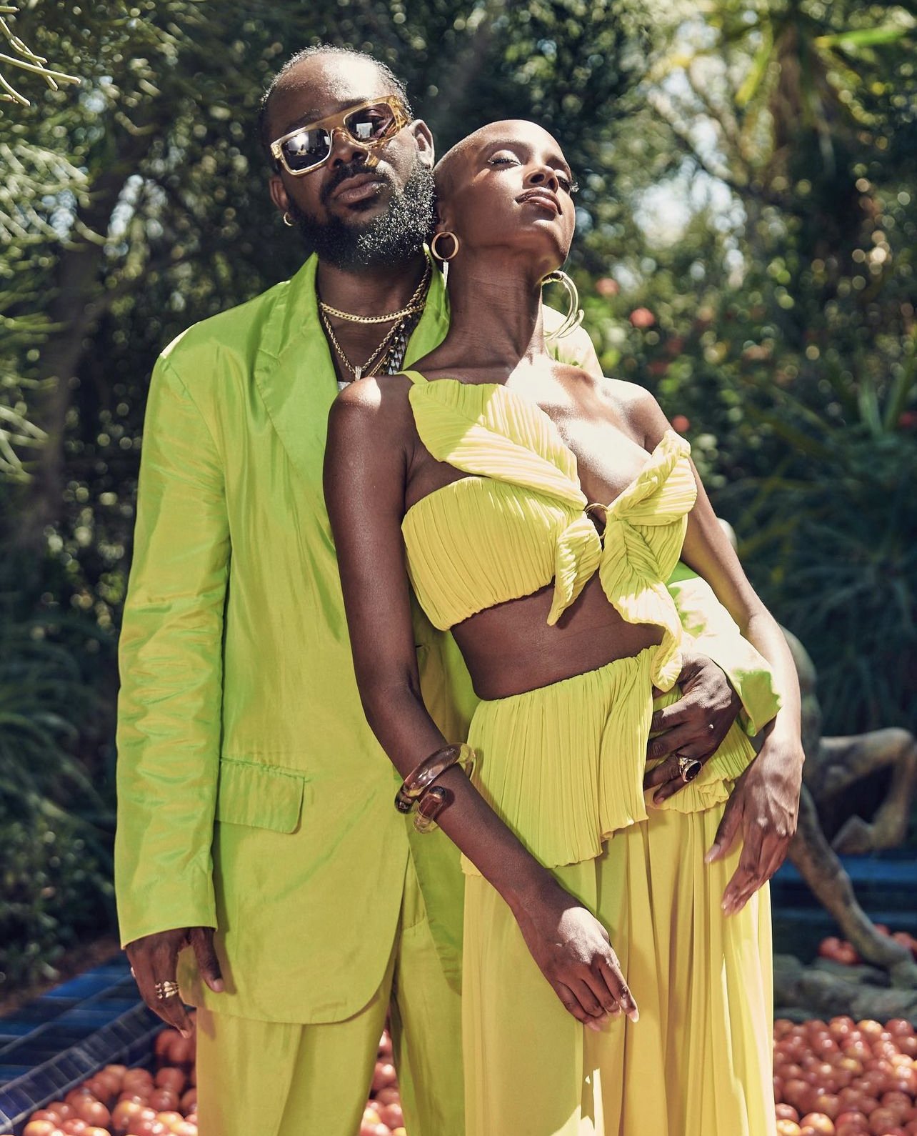 Stylish couple posing outdoors in matching neon green outfits, the woman in a crop top and wide-leg pants, the man in a suit.