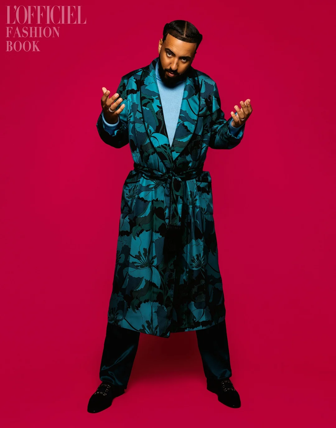 Full-length shot of adult male in patterned robe against magenta backdrop, arms outstretched in indoor studio setting for a fashion editorial.
