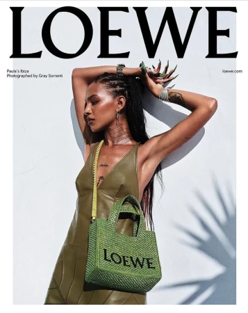 Woman in olive green leather dress holding a woven green tote bag against a white wall with palm tree leaf shadows