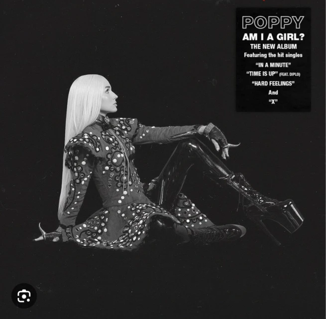 Black and white studio shot of a woman with long white hair wearing a dark dress with light circular patterns and platform boots.