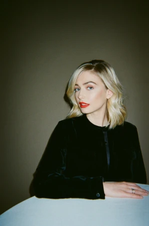 Portrait of a blonde woman wearing a black velvet top with red lipstick against a dark wall